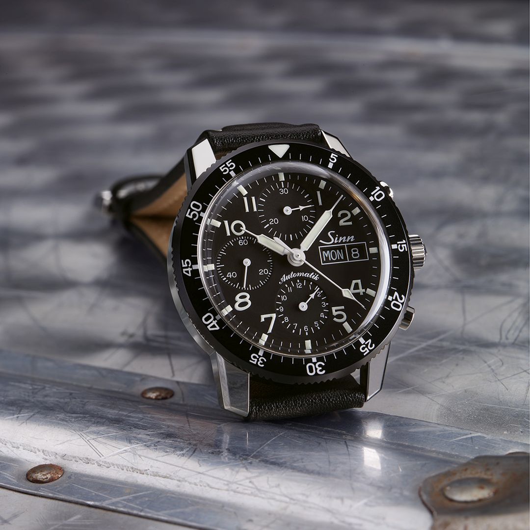 A stylish black watch resting on a polished metal surface, highlighting its modern aesthetic. Sinn 103_St_Classic_Pilot_watch - stainless steel - lather strap_band - swiss chronograph - wrist watch